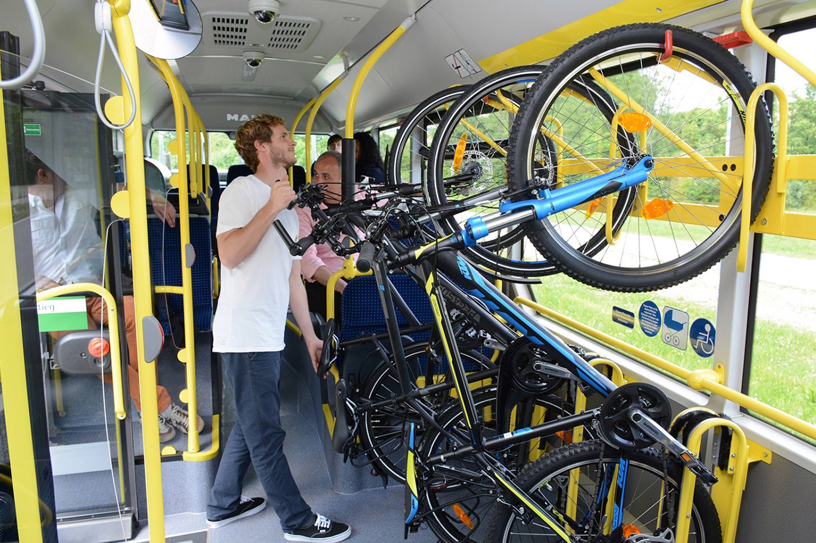Ein Mann hängt sein Fahrrad im Bus mit dem Vorderrad nach oben in eine Halterung.