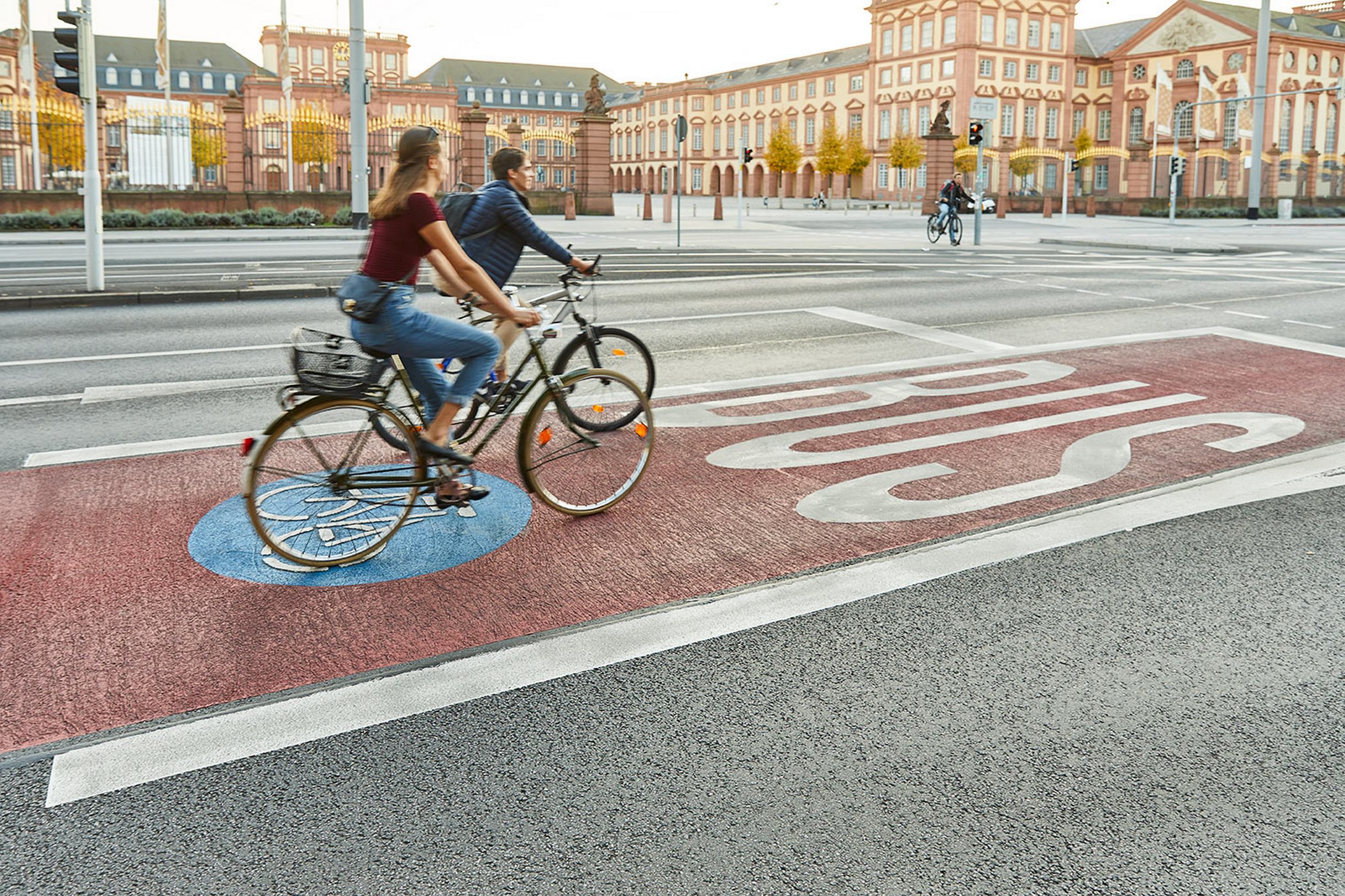 Zwei Fahrradfahrer auf der Radspur vor dem Schloss Mannheim.